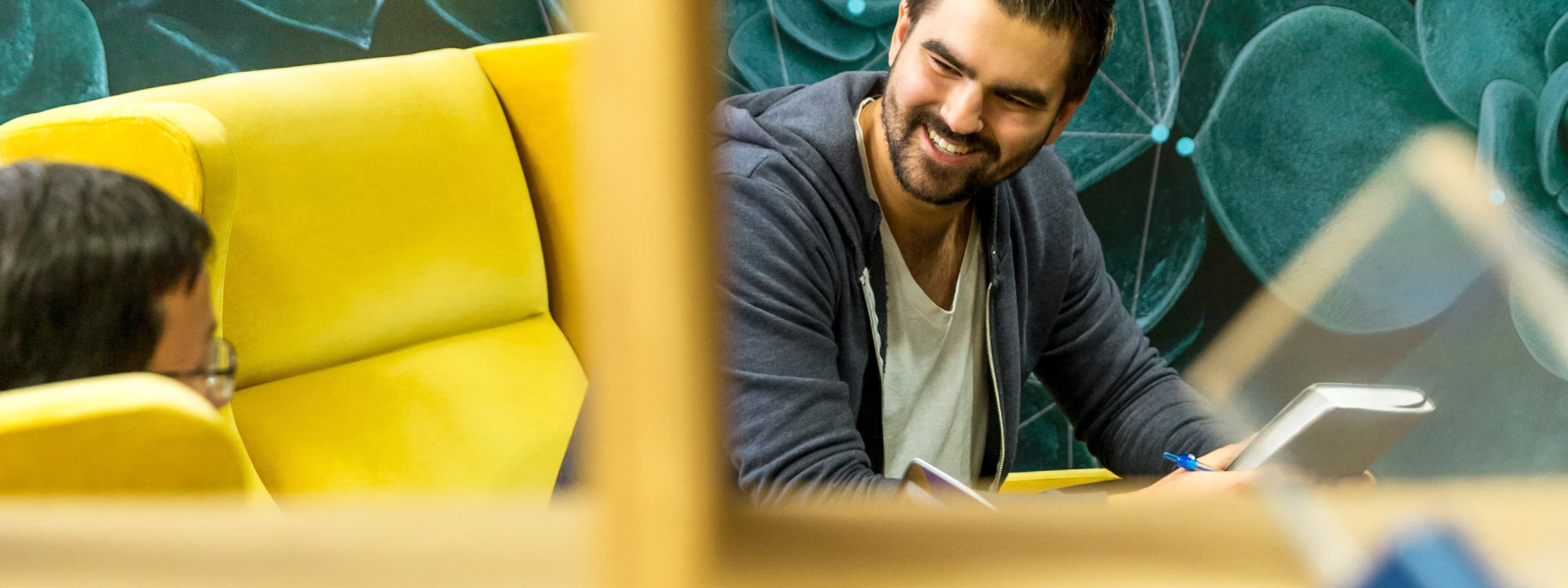 Smiling person working on tablet near yellow couch in modern office