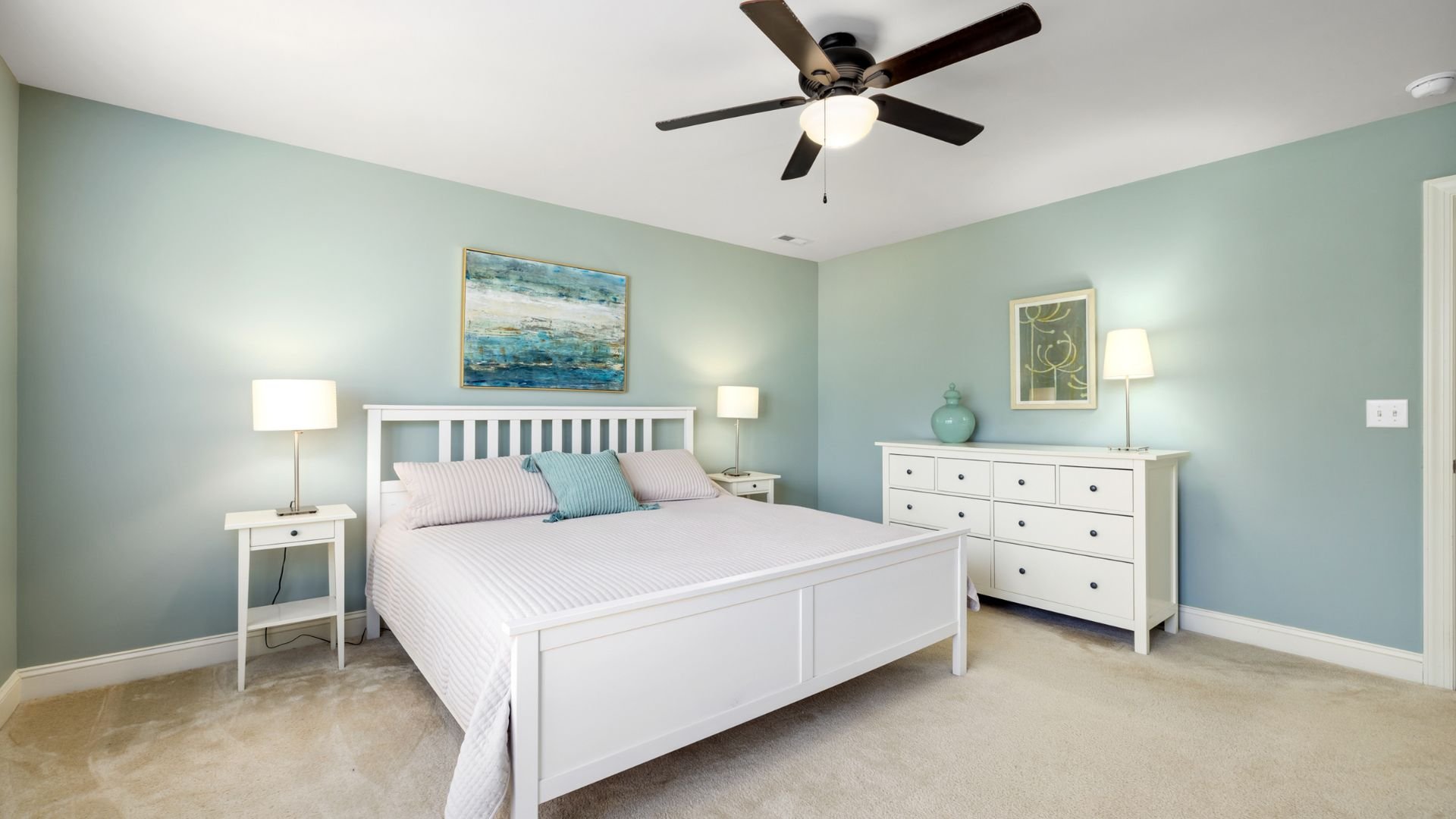Serene bedroom with white furniture, blue walls, and coastal artwork