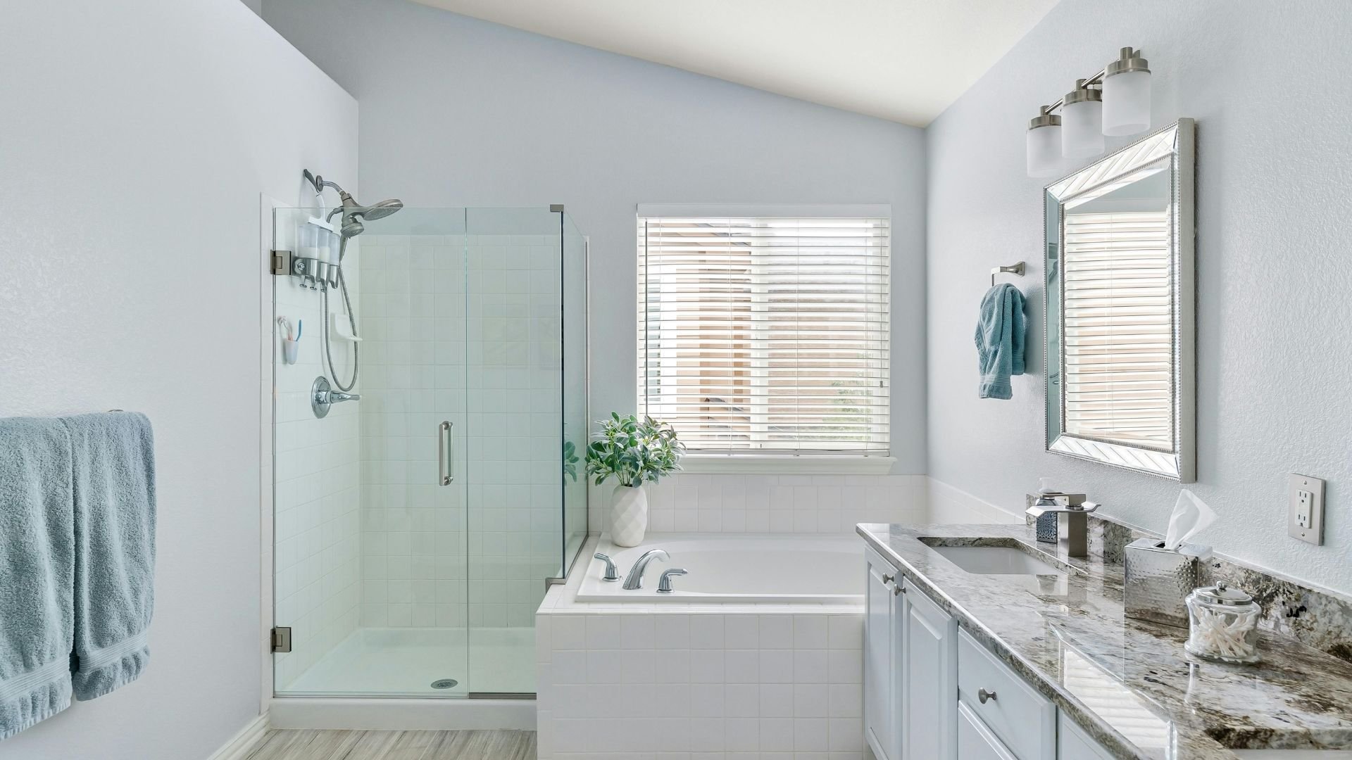 Modern bathroom with glass shower, white tub, and blue-gray accents