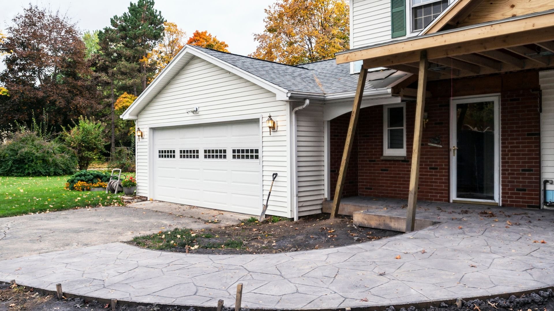 Autumn scene with white garage, brick house, and stone patio under construction