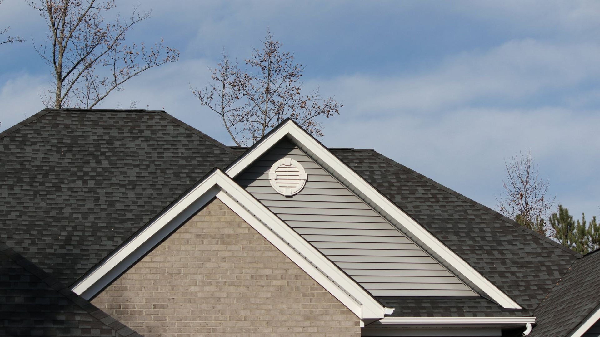 Residential roof with gray shingles, brick wall, and white trim